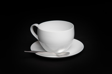 White coffee or tea cup with saucer and spoon and black backdrop
