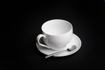White coffee or tea cup with saucer and spoon and black backdrop