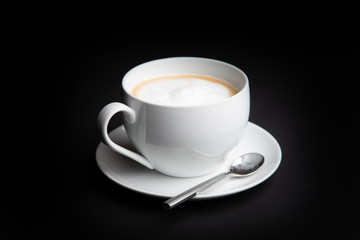 Cappuccino coffee in white cup with spoon and saucer and black backdrop
