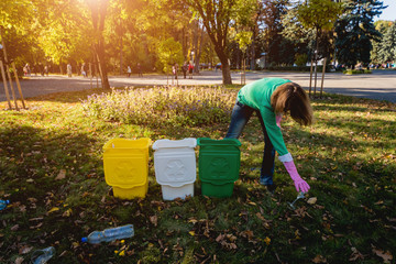 Volunteer girl sorts garbage in the street of the park. Concept of recycling.