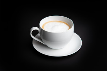 Cappuccino coffee in white cup with saucer and black backdrop