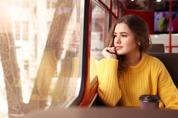 A young woman in a mustard sweater sits in a cafe and looks out the window, a woman drinking coffee