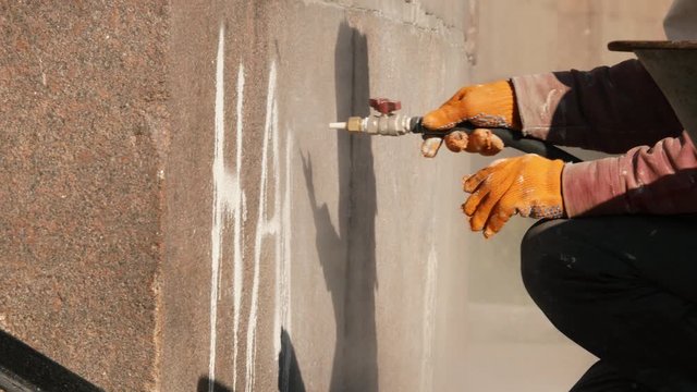 Worker removing graffiti with high pressure cleaner splashing. Cleaning wall using sandblaster gun. Professional cleaning services 4k
