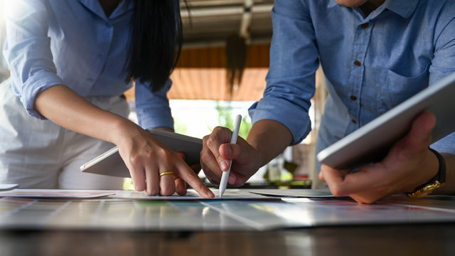 Cropped image of young graphic designer team holding/using a stylus pen and computer tablet while planning/brainstorming/discussing about their new project design at the modern meeting table.