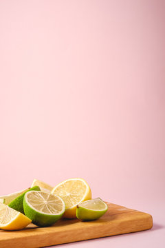 Naklejka Fresh tasty lemon and lime citrus fruits slices on wooden cutting board, minimal pink background isolated, angle view