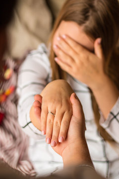 A man's hand holds a woman's hand. The girl has an engagement ring with a diamond. In the background, a smiling, happy girl, covering her eyes with her hand. Vertical photo. Concept: engagement, love