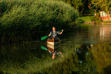 Ein Mann paddelt am Frühen Morgen in einem Kanu auf einem Fluss im Grünen