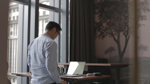 asian man works on laptop stand desk behind angle