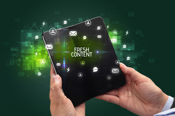 Businessman holding a foldable smartphone with FRESH CONTENT inscription, social networking concept