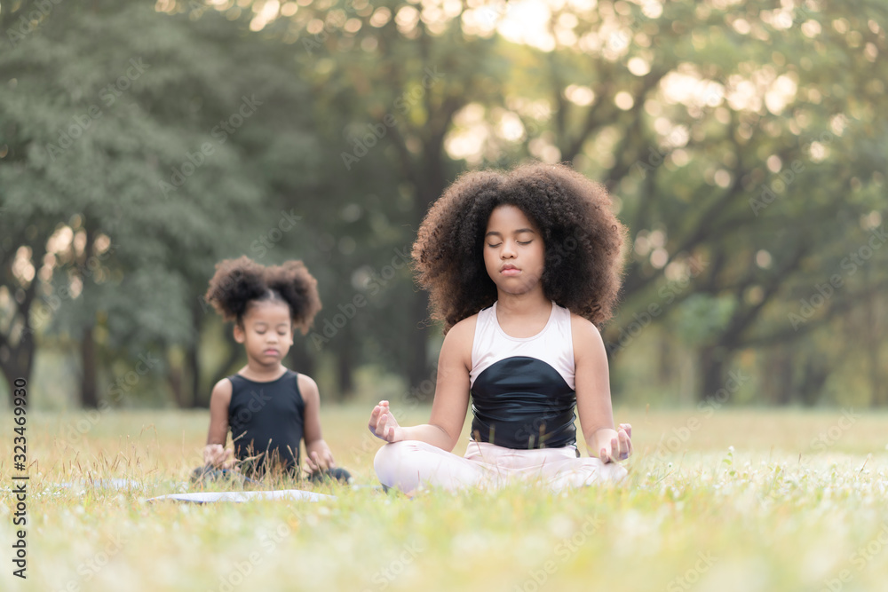 Wall mural African american little girl sitting on the roll mat practicing meditate yoga in the park outdoor