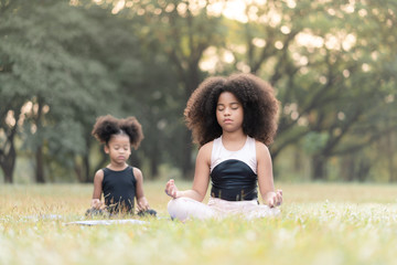 African american little girl sitting on the roll mat practicing meditate yoga in the park outdoor