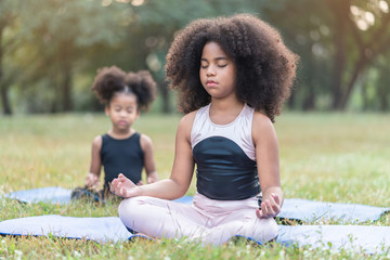 African american little girl sitting on the roll mat practicing meditate yoga in the park outdoor - obrazy, fototapety, plakaty