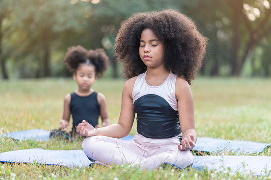 African american little girl sitting on the roll mat practicing meditate yoga in the park outdoor