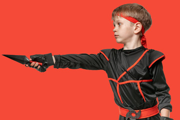 Fototapeta na wymiar Portrait of young ninja boy training with kunai to attack the enemy on red background
