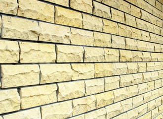 Side view of a yellow wall of rectangular tiles of rough stone.