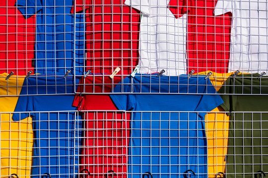 Rows of many multi colored T-shirts hanging on white grille mesh clothes rack for sale in clothing store in outdoor market