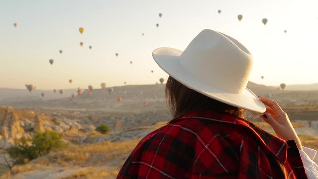 Woman in hat walking in Cappadocia. Colorful hot air balloons flying over the valley in Cappadocia, Turkey