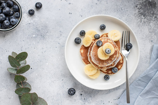 Tasty pancakes with fresh blueberries, banana and powdered sugar on a gray concrete background. horizontal image, top view, place for text