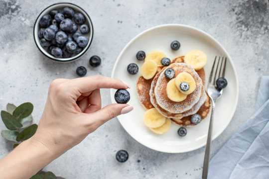 woman's hand holding fresh blueberries on a table with a pancake. horizontal image, top view