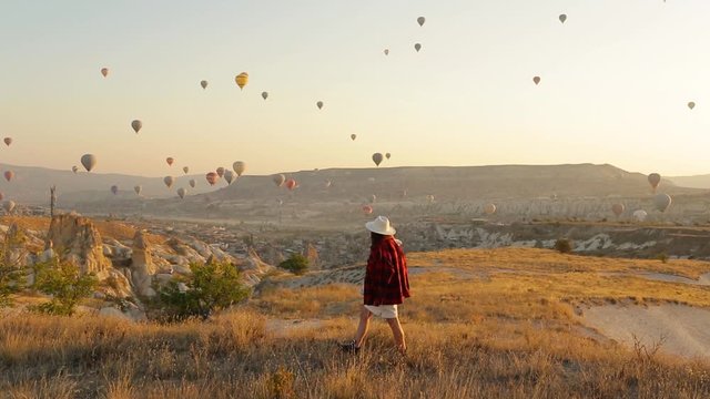 Woman in hat walking in Cappadocia. Colorful hot air balloons flying over the valley in Cappadocia, Turkey