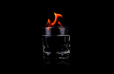 Glass with vodca and fire flame on black background