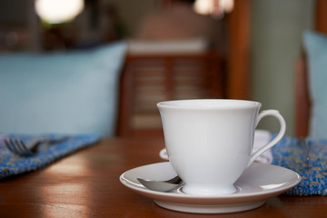 White cup of tea or hot coffee with spoon on blur table dining background