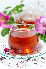 fragrant tea with wild rose in a glass cup on a white table, vertical closeup