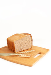 Half a loaf of rye-wheat bread on a cutting board with ears of wheat. Bread, food