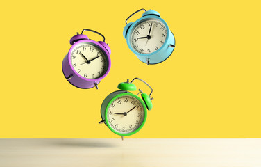 Multicolored alarm clocks flying over the table on yellow background. Copy space