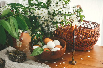Natural Easter eggs, vintage candle and wicker basket on rustic table with cherry flowers and green...