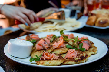 Fried pies with red fish and sour cream on a plate. In the background - hands, pancakes, pies