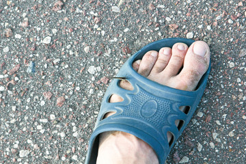 The butterfly sat on the foot of a man dressed in flip flops against the asphalt pavement in the...