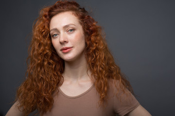 Happy curly red-haired woman with a beautiful smile, looking directly at the camera. On an isolated gray background. The concept of happiness and emotions