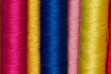 Vertical placed cones of bright colored sewing thread with yellow and pink cones in background