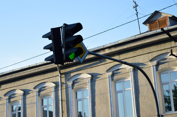 Street traffic light with green light on the background of the sky and building