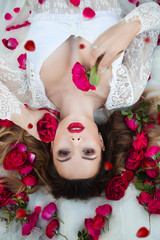 Loving girl. The girl in a red dress lying on the floor in the petals of roses.