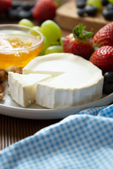 Cheese plate round sliced soft cheese, blueberry, strawberry, grapes and honey on wooden table.