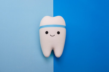 Cheerful smiling tooth on a blue background with copy space. Pediatric and adult dentistry. Dental treatment and whitening.