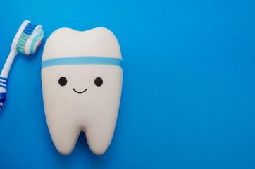 Cheerful smiling tooth on a blue background with a toothbrush with copy space. Pediatric and adult dentistry. Dental treatment and whitening.