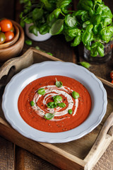 Bowl of tomato soup with a basil on wooden background