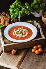 Bowl of tomato soup with a basil on wooden background