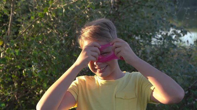Closeup view 4k video portrait of cute funny face of white kid playing cheerfully outdoor and looking through pink circle made of slime toy.