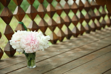 A bouquet of pink peonies stand in a glass vase against the background of a wooden table and a...