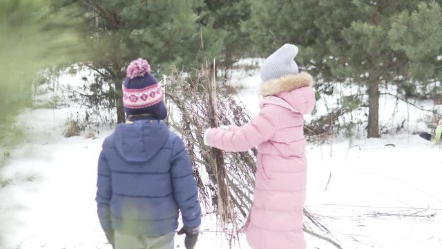 Children build a house from branches in the winter forest. Children's game with natural material in winter on the street