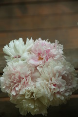 A bouquet of pink peonies stand in a glass vase against the background of a brown wooden floor