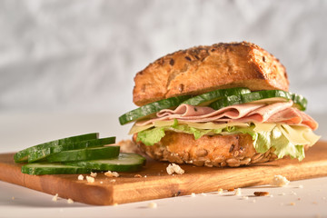 sandwich with meat, salad, cucumbers on a wooden surface
