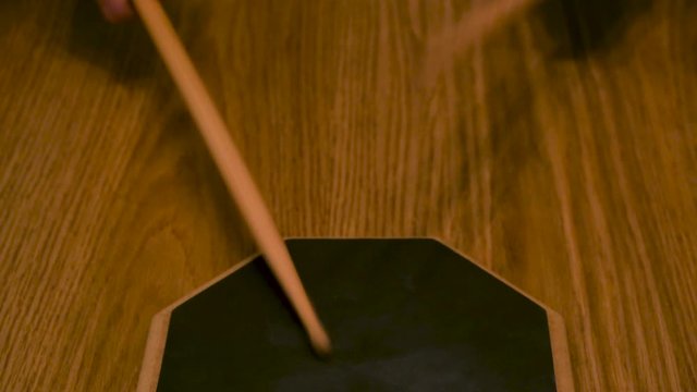 Close up of a man or woman practicing on a drum pad with drumsticks on wooden table background. Concept. A person is training to beat the rhythm.