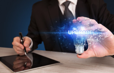 Businessman holding light bulb with UPGRADE inscription, innovative technology concept