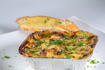 Chicken lasagna with garlic bread, baked in aluminum plate, white background