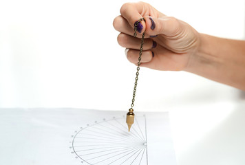 Arm of dowser with hand-held pendulum over the chart. Selective focus. - obrazy, fototapety, plakaty